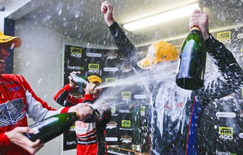 Garth Tander gives Shane van Gisbergen a spray on the Hamilton podium – van Gisbergen